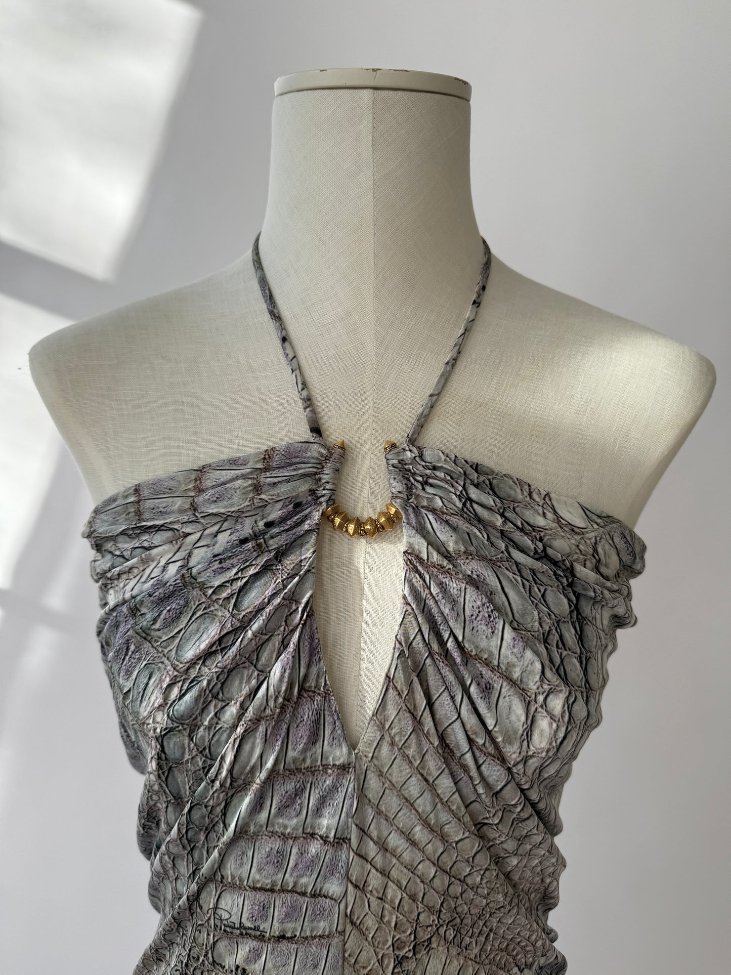 Extreme close-up of crocodile texture and gold hardware on Cavalli mini dress displayed on mannequin.