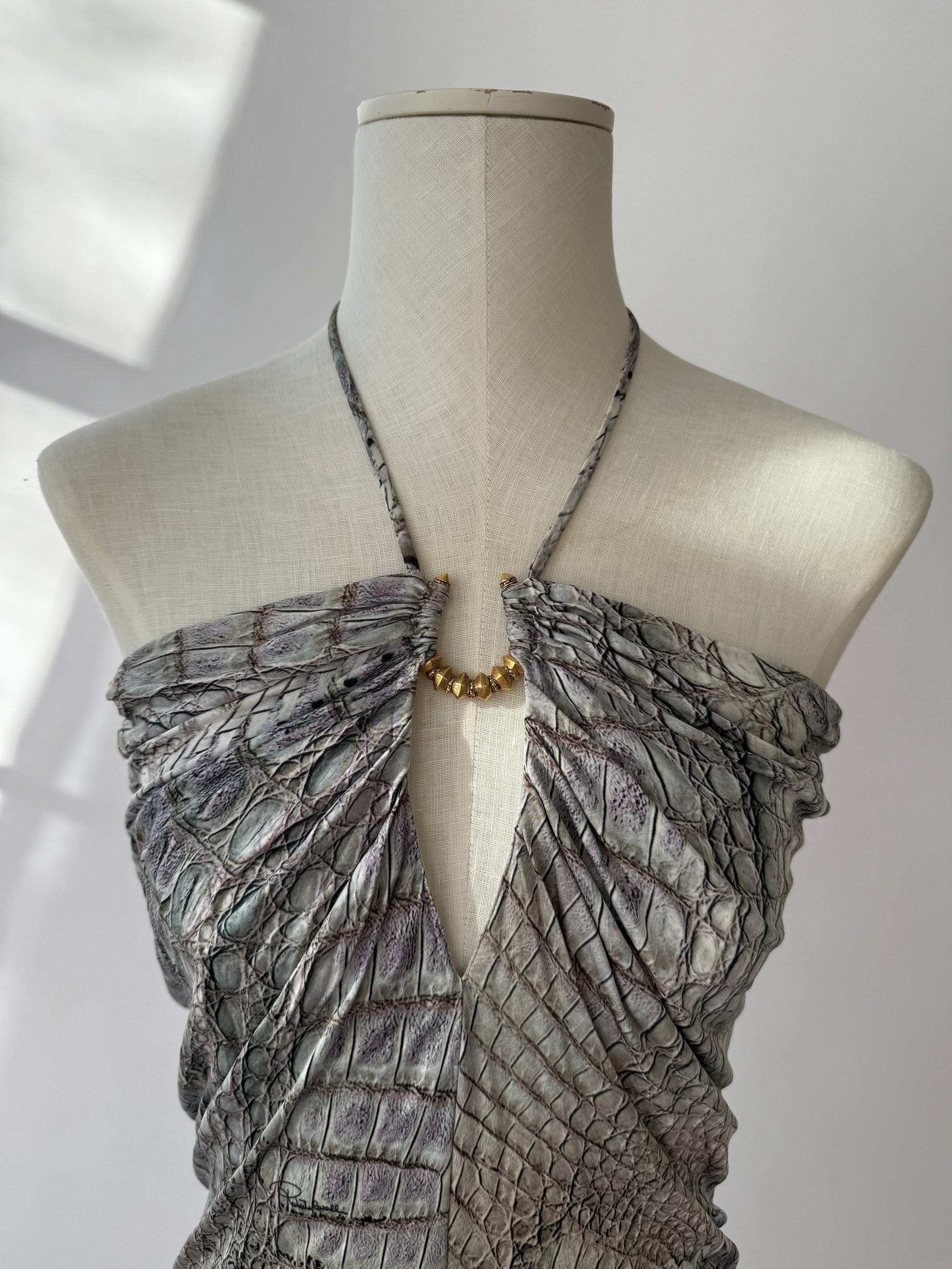 Extreme close-up of crocodile texture and gold hardware on Cavalli mini dress displayed on mannequin.