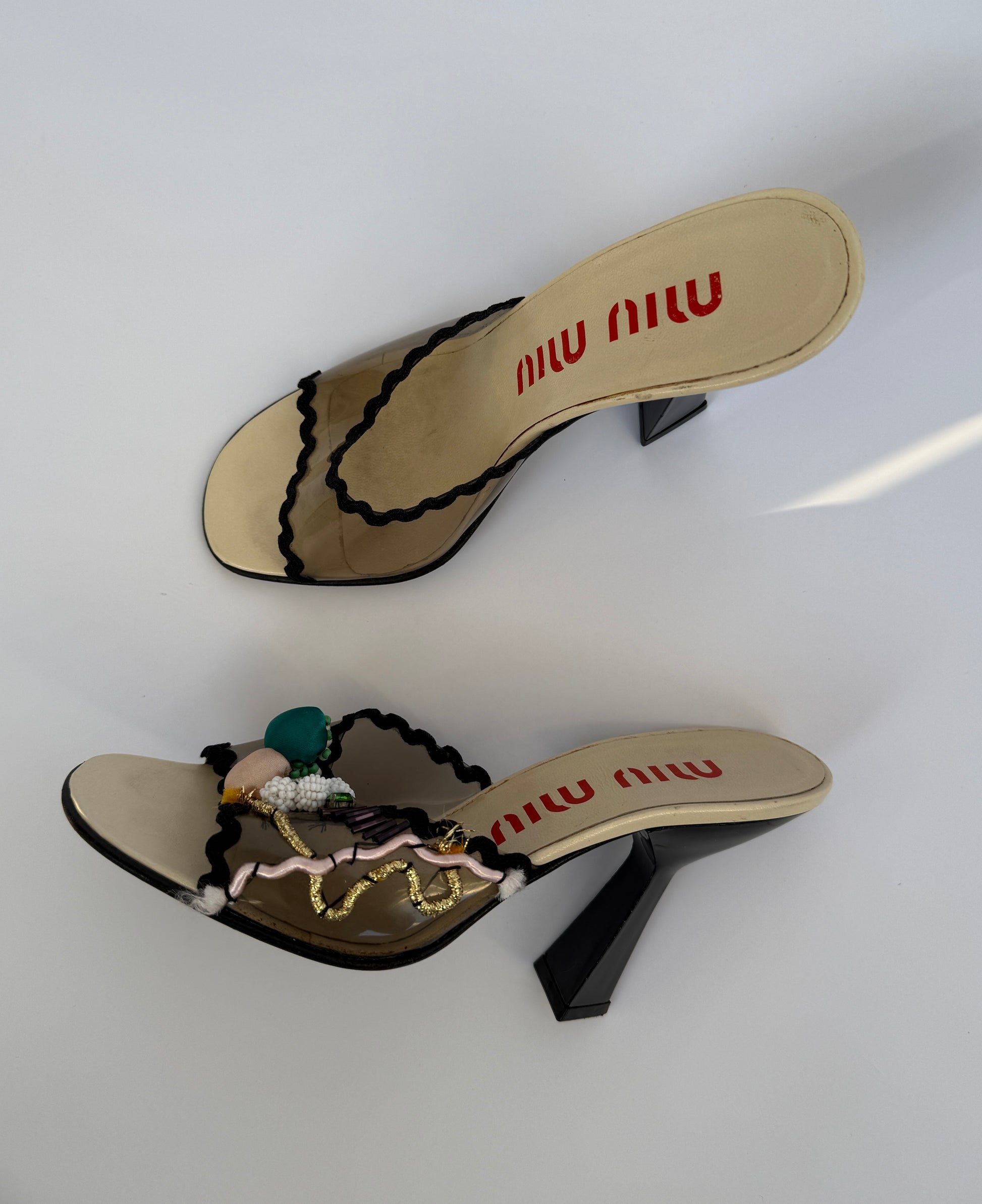 Top view of the Miu Miu S/S 1998 Clear PVC Embroidered Black Squiggle Mules, while one heel is laying down and the other is straight up.