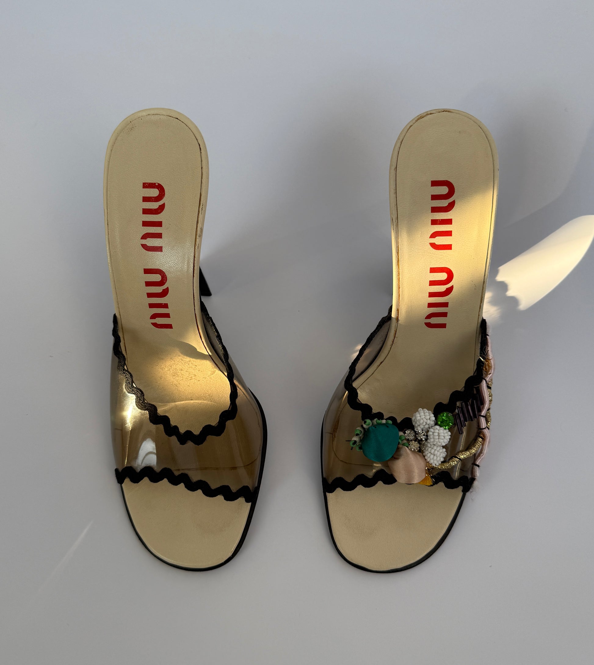 The Miu Miu S/S 1998 Clear PVC Embroidered Black Squiggle Mules seen from the top with a ray of sunlight highlighting the mules.